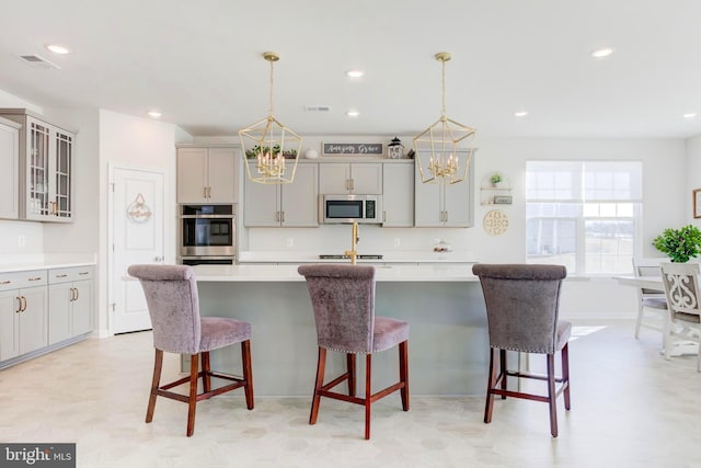 kitchen featuring stainless steel appliances, gray cabinets, an island with sink, and hanging light fixtures