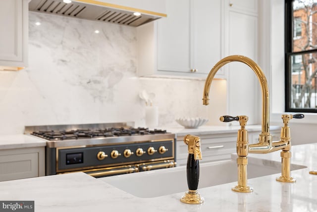 kitchen with ventilation hood, range with two ovens, backsplash, and white cabinets