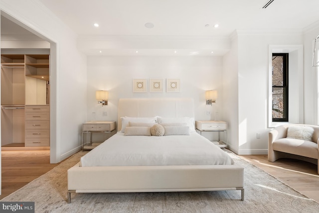 bedroom featuring baseboards, ornamental molding, a walk in closet, light wood-type flooring, and recessed lighting