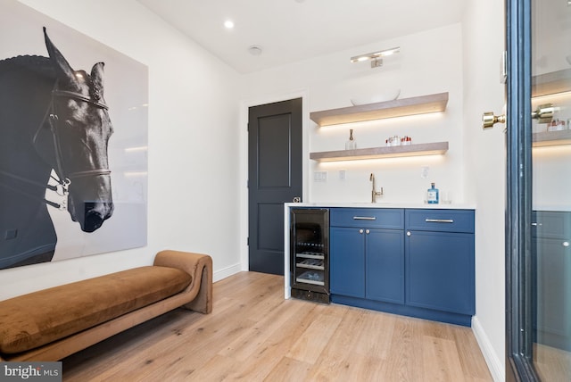 bar with beverage cooler, baseboards, wet bar, light wood-type flooring, and a sink