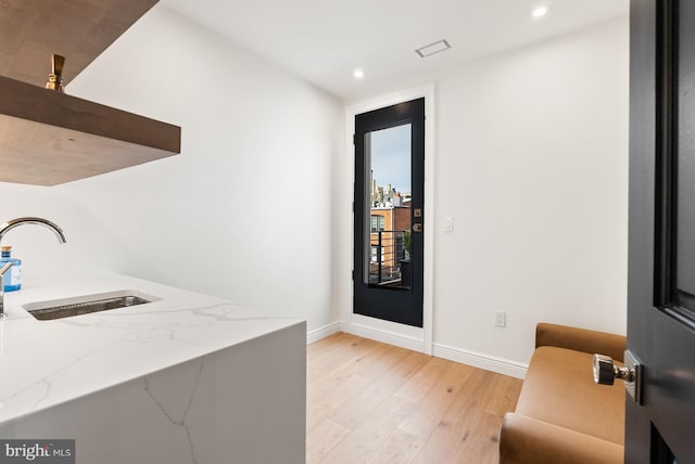 interior space featuring light wood-style floors, baseboards, light stone counters, and a sink