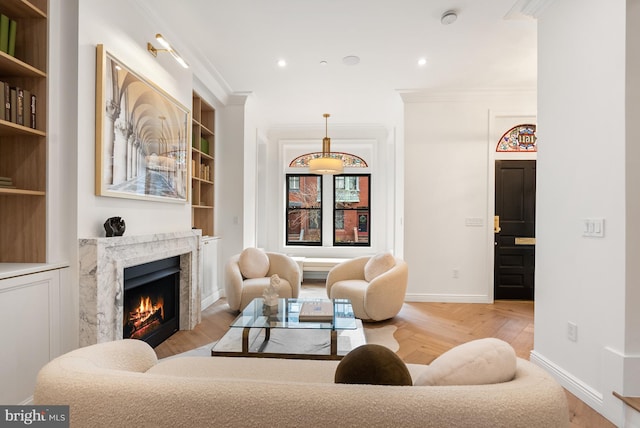 living area featuring built in features, a fireplace, baseboards, and crown molding