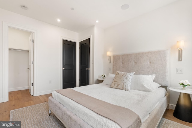 bedroom with a walk in closet, recessed lighting, baseboards, and wood finished floors