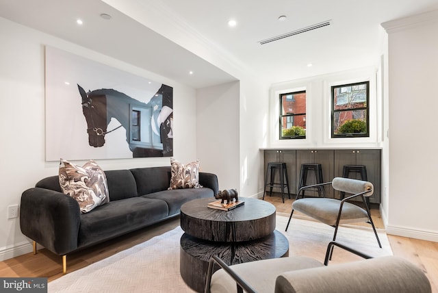 living area featuring light wood-type flooring, visible vents, and crown molding