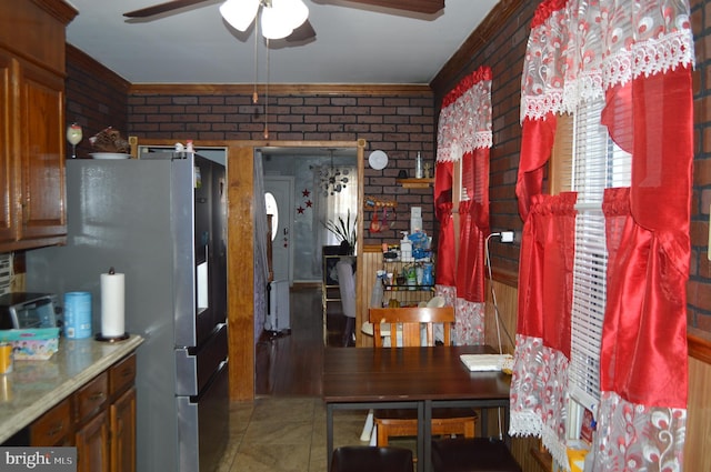 kitchen featuring stainless steel refrigerator, ceiling fan, and brick wall