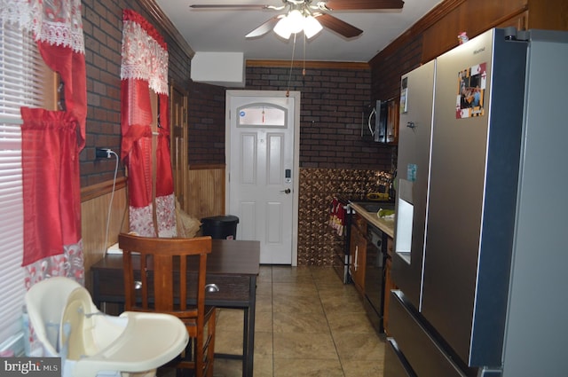 kitchen with ceiling fan, tile patterned floors, brick wall, and appliances with stainless steel finishes