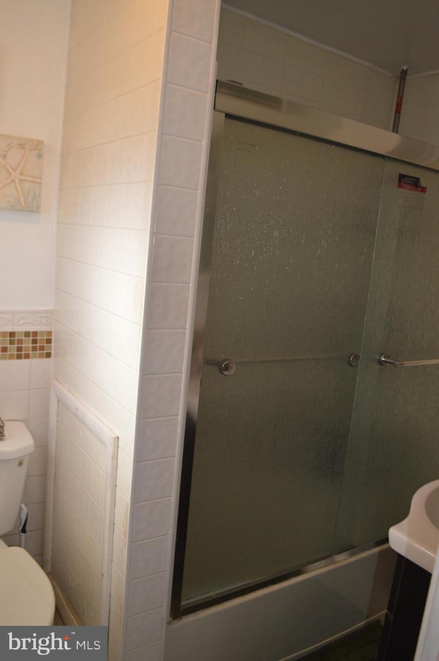 bathroom with vanity, toilet, a shower with shower door, and tile walls