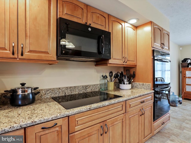 kitchen featuring black appliances, light stone counters, and a textured ceiling