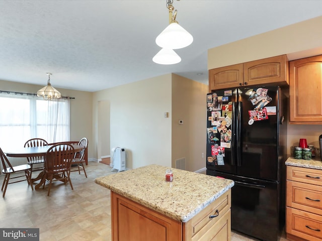 kitchen featuring a center island, visible vents, freestanding refrigerator, light stone countertops, and pendant lighting