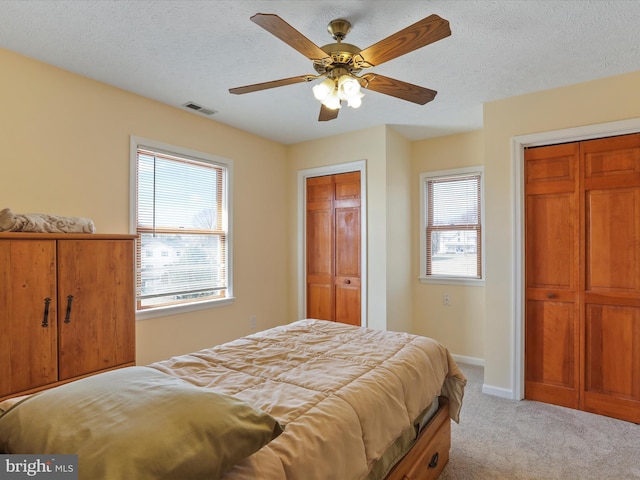 bedroom featuring two closets, visible vents, light carpet, a textured ceiling, and baseboards