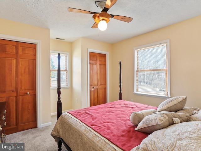 bedroom with two closets, visible vents, light carpet, a textured ceiling, and baseboards