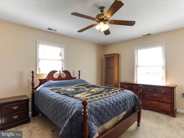 bedroom featuring a textured ceiling, a ceiling fan, visible vents, and light colored carpet