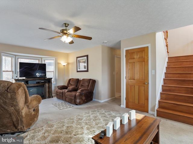 carpeted living room with baseboards, a glass covered fireplace, ceiling fan, stairway, and a textured ceiling