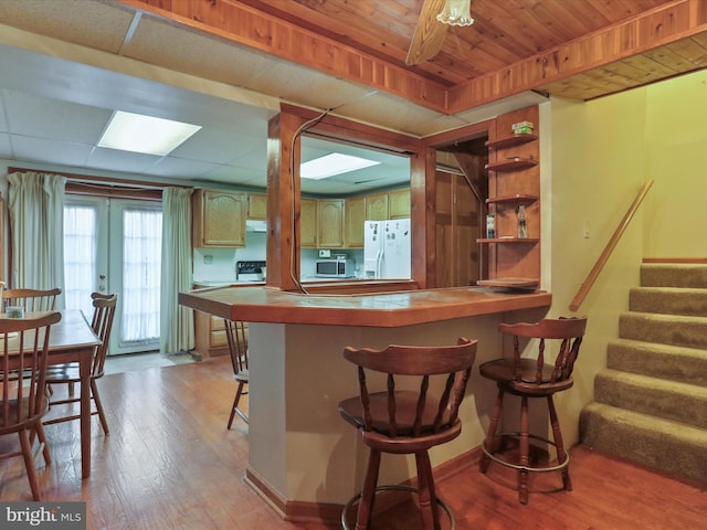 kitchen with a breakfast bar, wood finished floors, french doors, white fridge with ice dispenser, and stainless steel microwave