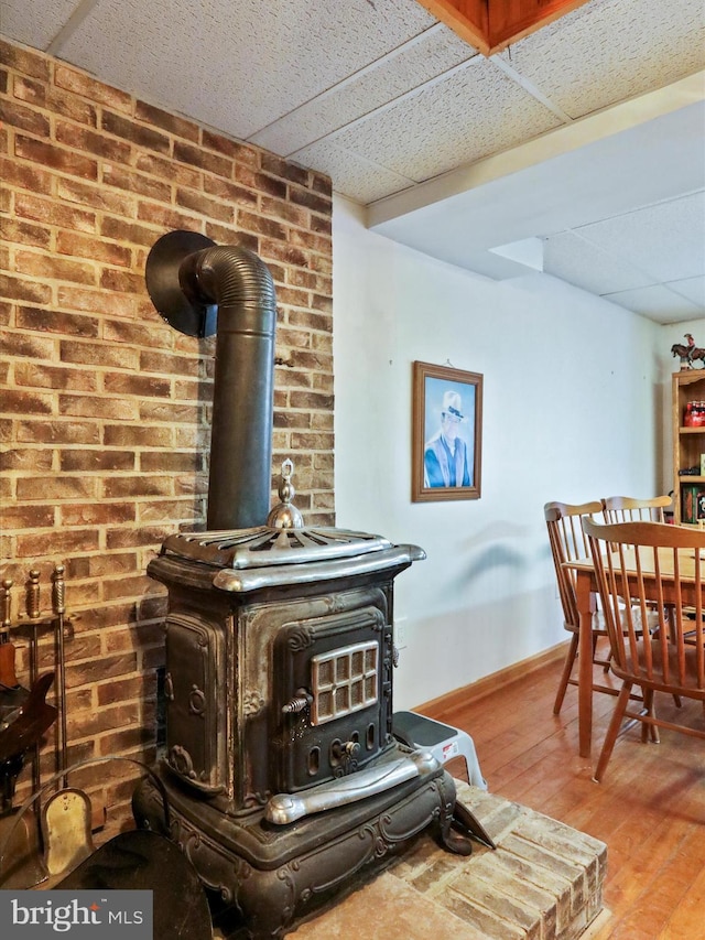 room details with a drop ceiling, wood finished floors, a wood stove, and baseboards