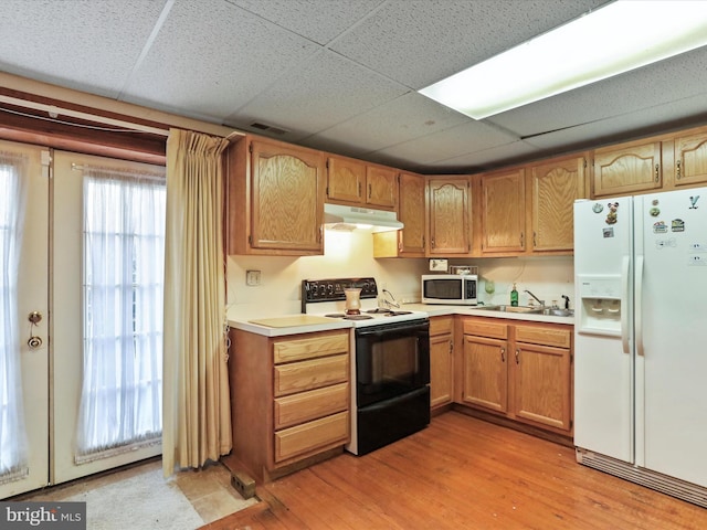 kitchen with under cabinet range hood, white appliances, a sink, light countertops, and light wood-type flooring