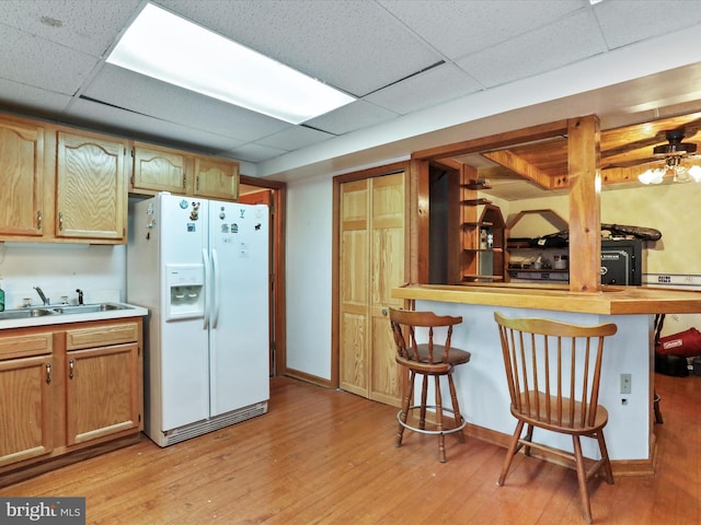 kitchen featuring white refrigerator with ice dispenser, a sink, light wood-type flooring, a drop ceiling, and a kitchen breakfast bar