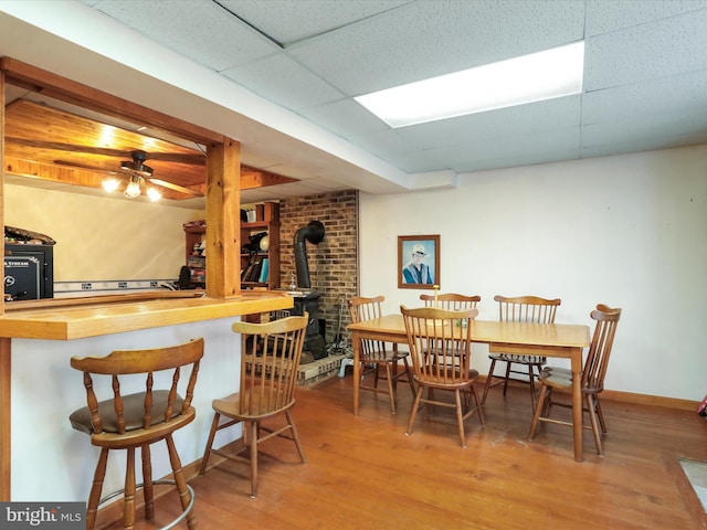 dining area with a dry bar, ceiling fan, wood finished floors, a wood stove, and a paneled ceiling