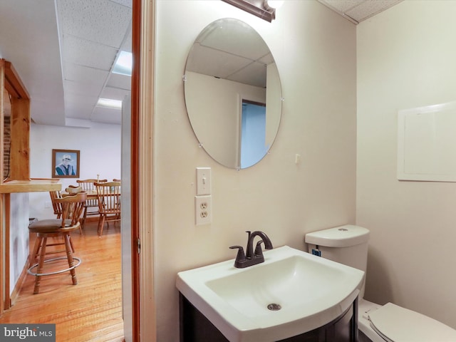 bathroom featuring toilet, vanity, wood finished floors, and a paneled ceiling