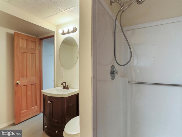 bathroom with toilet, a walk in shower, a drop ceiling, and vanity