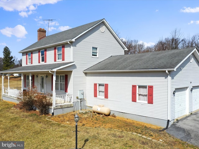 view of front facade with driveway, a chimney, roof with shingles, a porch, and a front yard