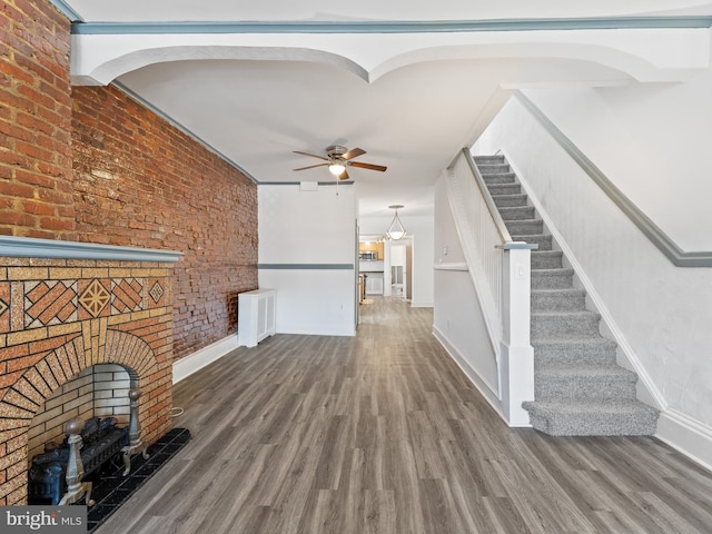 unfurnished living room featuring ceiling fan, a fireplace, wood-type flooring, and brick wall