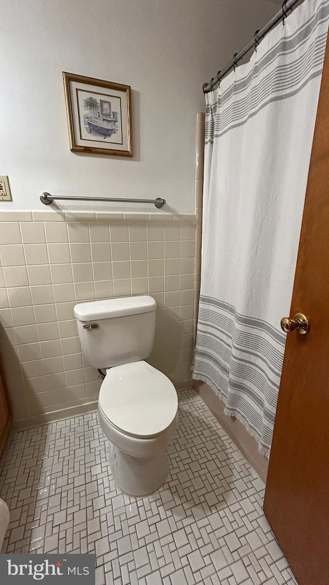 full bath featuring toilet, a shower with curtain, a wainscoted wall, and tile walls