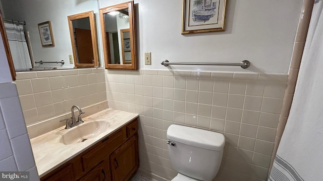 full bathroom with tile walls, toilet, vanity, and a wainscoted wall