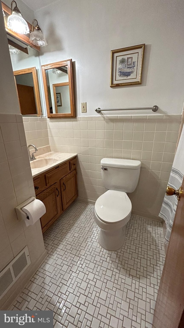 bathroom featuring wainscoting, vanity, tile walls, toilet, and visible vents