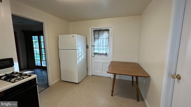 kitchen with range with gas cooktop, freestanding refrigerator, baseboards, and light floors