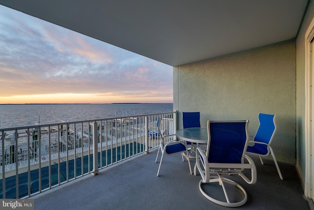 balcony at dusk featuring a water view