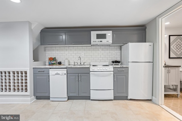 kitchen with light tile patterned floors, gray cabinets, decorative backsplash, a sink, and white appliances