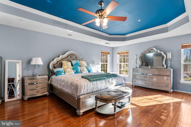 bedroom with dark hardwood / wood-style floors, ceiling fan, ornamental molding, and a tray ceiling