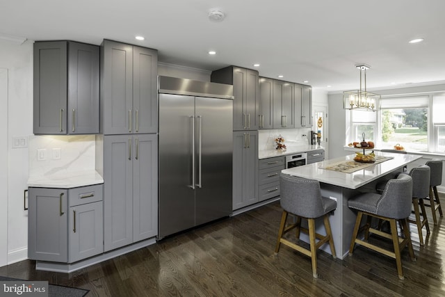 kitchen with a breakfast bar area, appliances with stainless steel finishes, gray cabinetry, hanging light fixtures, and light stone countertops