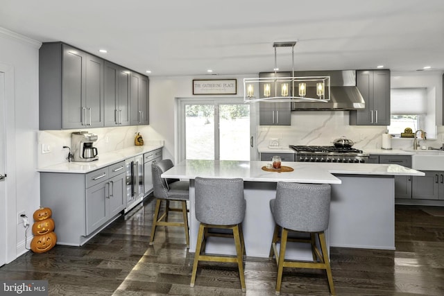 kitchen with wall chimney exhaust hood, gray cabinetry, decorative light fixtures, a center island, and stainless steel gas stovetop