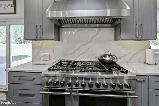 kitchen with gray cabinets, double oven range, wall chimney range hood, and light stone counters