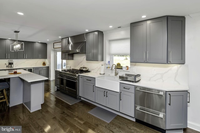 kitchen featuring wall chimney exhaust hood, sink, hanging light fixtures, gray cabinets, and range with two ovens