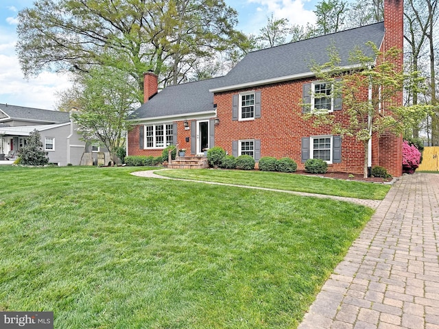 view of front facade with roof with shingles, brick siding, a chimney, and a front yard