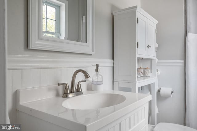 bathroom featuring a wainscoted wall, toilet, and vanity