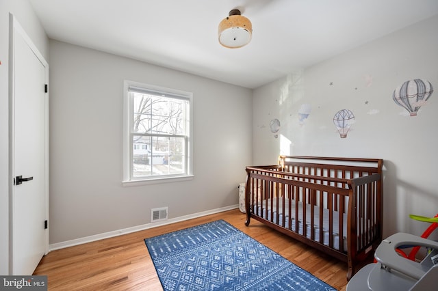 bedroom featuring a nursery area, baseboards, visible vents, and wood finished floors