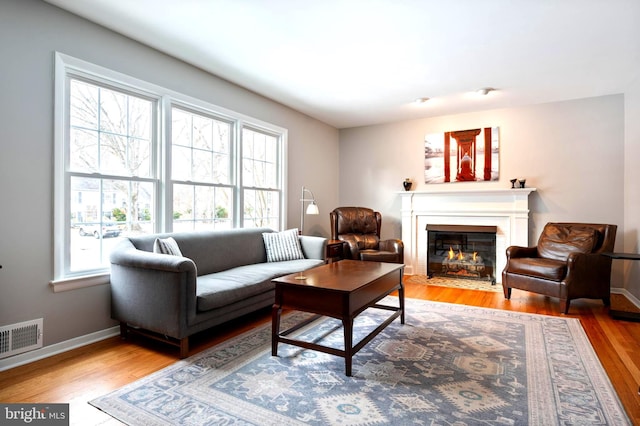 living room featuring a fireplace with flush hearth, visible vents, baseboards, and wood finished floors