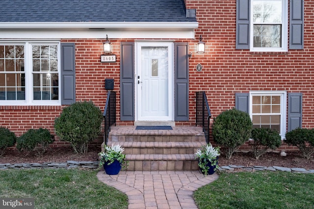 property entrance featuring a shingled roof and brick siding