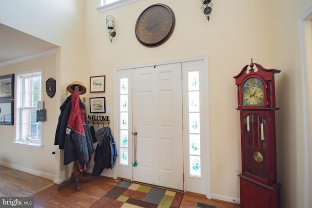 foyer entrance featuring crown molding, wood finished floors, baseboards, and visible vents