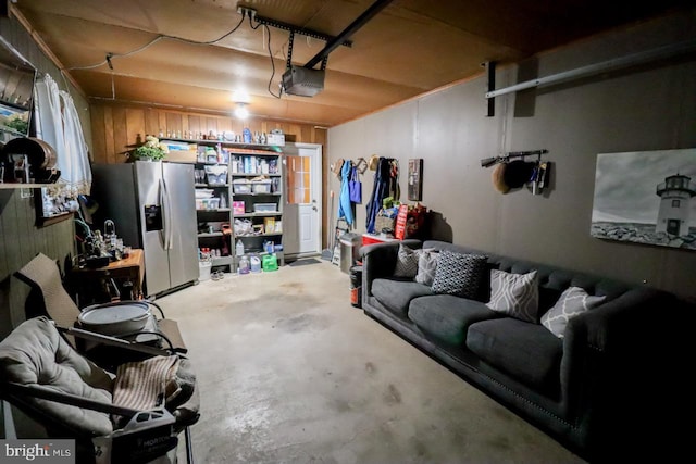 garage with stainless steel fridge with ice dispenser, a garage door opener, and wood walls