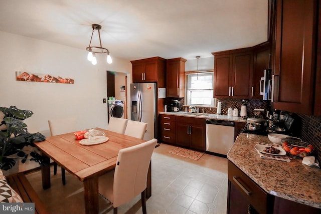 kitchen featuring stainless steel appliances, tasteful backsplash, light stone countertops, washer / dryer, and decorative light fixtures