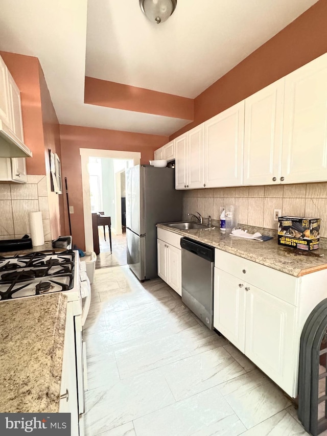 kitchen with stainless steel appliances, white cabinetry, sink, and light stone counters