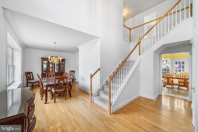 dining space with crown molding, a notable chandelier, a towering ceiling, and light hardwood / wood-style flooring