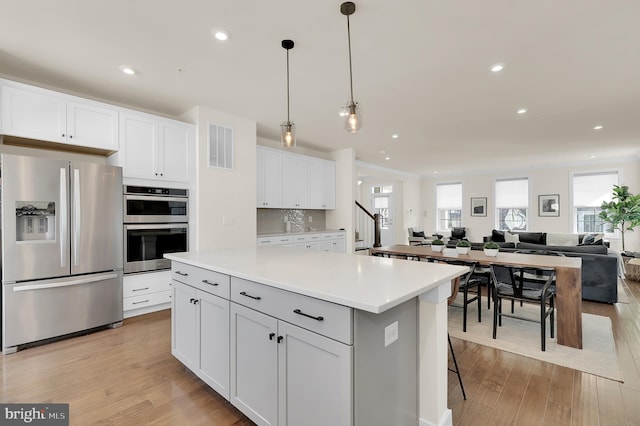 kitchen with a center island, stainless steel appliances, light countertops, open floor plan, and white cabinetry