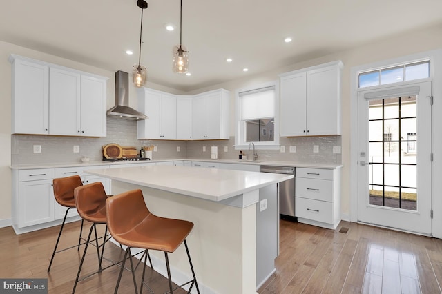 kitchen with wall chimney exhaust hood, a kitchen island, light countertops, stainless steel appliances, and white cabinetry