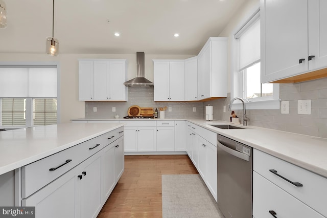 kitchen with stainless steel appliances, a sink, white cabinetry, light countertops, and wall chimney exhaust hood